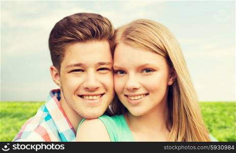holidays, vacation, love and people concept - smiling teenage couple hugging over blue sky and grass background