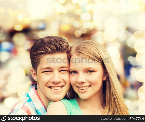 holidays, vacation, love and people concept - smiling teenage couple hugging over holiday lights background