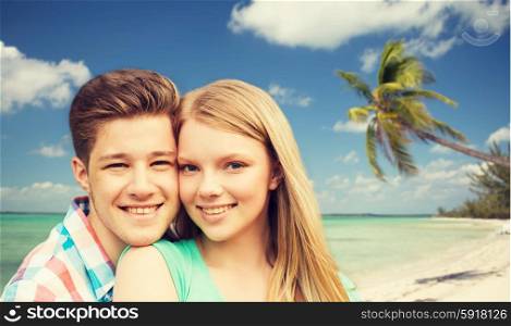 holidays, vacation, love and people concept - smiling teenage couple hugging over tropical beach background