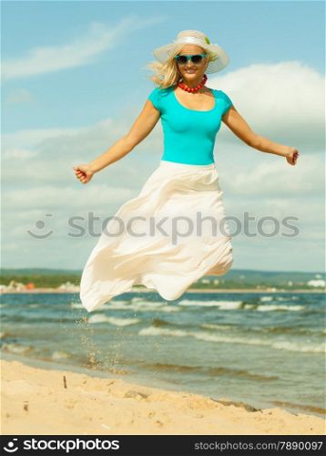 Holidays, vacation travel and freedom concept. Beautiful girl in summer clothing hat jumping on beach. Young woman having fun relaxing on the sea coast.