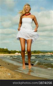 Holidays, vacation travel and freedom concept. Beautiful girl in white dress jumping on beach. Young woman having fun relaxing on the sea coast.