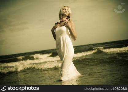 Holidays, vacation travel and freedom concept. Beautiful girl in white dress posing on beach. Young woman relaxing on the sea coast.