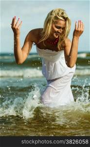 Holidays, vacation travel and freedom concept. Beautiful girl in white dress splashing water on beach. Young woman having fun relaxing on the sea coast.