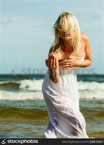 Holidays, vacation travel and freedom concept. Beautiful girl in white dress splashing water on beach. Young woman having fun relaxing on the sea coast.