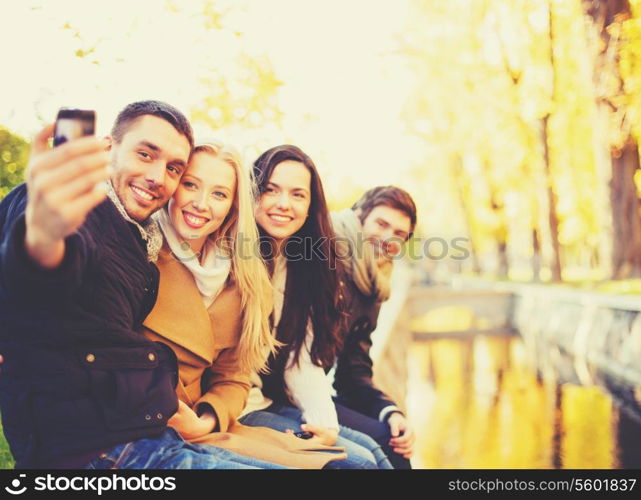 holidays, vacation, travel and tourism concept - group of friends or couples having fun in autumn park and taking selfie