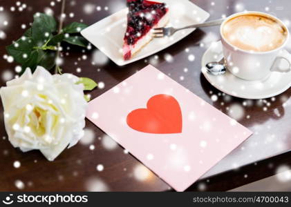 holidays, valentines day and love concept - close up of greeting card with heart, flower, cake and coffee over snow