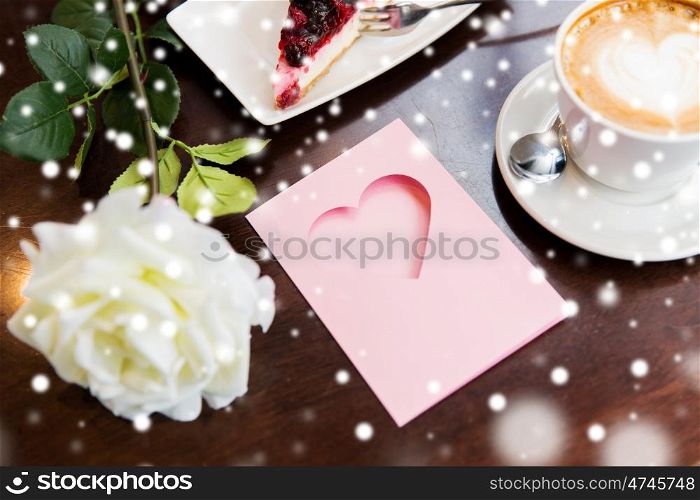holidays, valentines day and love concept - close up of greeting card with heart, flower, cake and coffee over snow