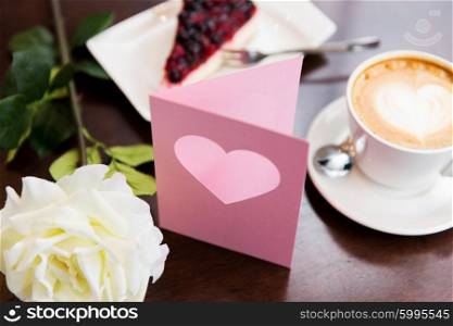 holidays, valentines day and love concept - close up of greeting card with heart, flower, cake and coffee
