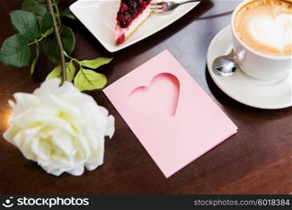 holidays, valentines day and love concept - close up of greeting card with heart, flower, cake and coffee