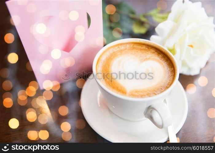 holidays, valentines day and love concept - close up of greeting card with heart, flower and coffee over holidays lights
