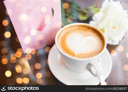holidays, valentines day and love concept - close up of greeting card with heart, flower and coffee over holidays lights