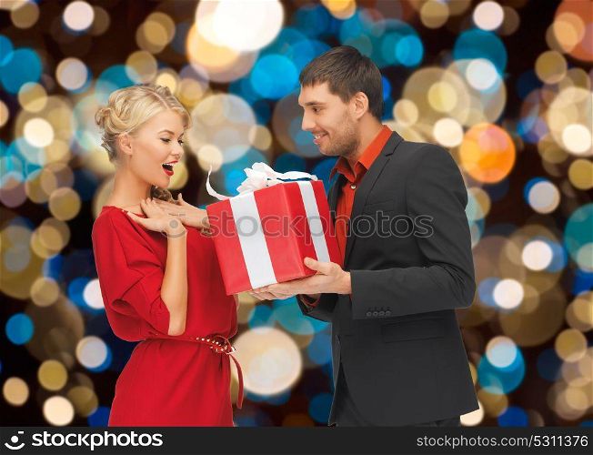 holidays, valentines day, christmas and people concept - happy couple with present over lights background. happy couple with christmas gift