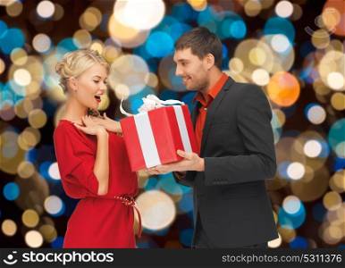 holidays, valentines day, christmas and people concept - happy couple with present over lights background. happy couple with christmas gift