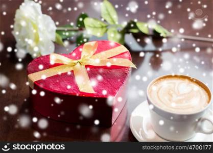 holidays, valentines day, love and drinks concept - close up of gift box, coffee cup and flower on table over snow