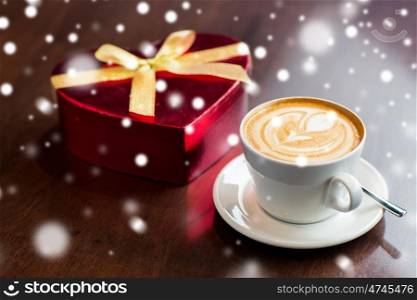 holidays, valentines day, love and drinks concept - close up of gift box and coffee cup on table over snow