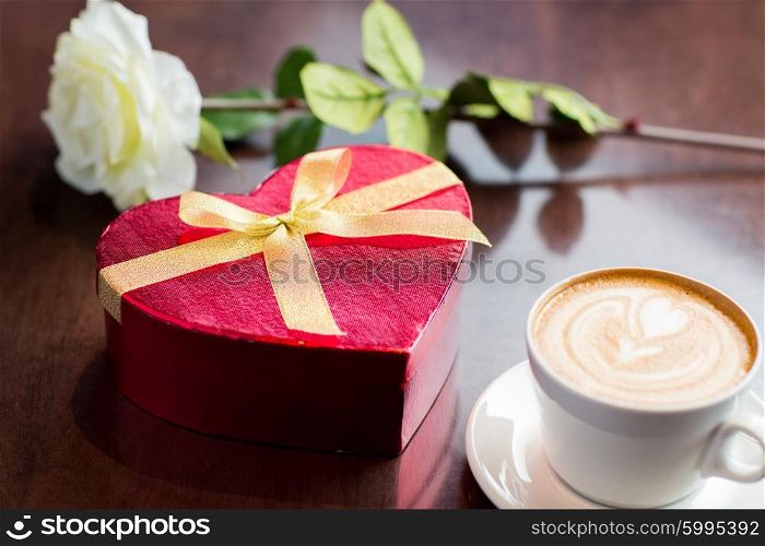 holidays, valentines day, love and drinks concept - close up of gift box, coffee cup and flower on table