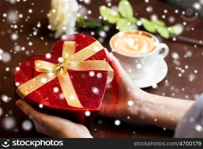 holidays, valentines day, love and people concept - close up of hands holding heart shaped gift box over snow