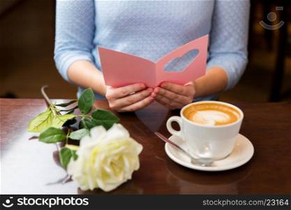 holidays, valentines day, people and love concept - close up of woman reading greeting card with heart, flower and coffee