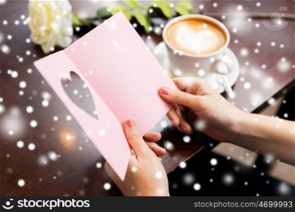 holidays, valentines day, people and love concept - close up of woman reading greeting card with heart, flower and coffee over snow