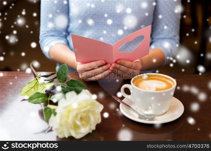 holidays, valentines day, people and love concept - woman reading greeting card with heart, flower and coffee cup over snow