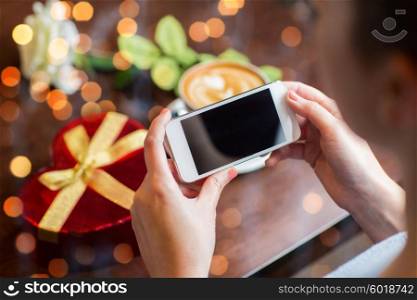 holidays, valentines day, technology and people concept - close up of hands with smartphone, gift box and coffee cup over holidays lights