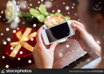 holidays, valentines day, technology and people concept - hands with smartphone, gift box and coffee cup over snow