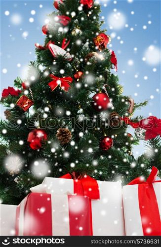 holidays, winter and celebration concept - close up of christmas tree and presents over blue background with snow
