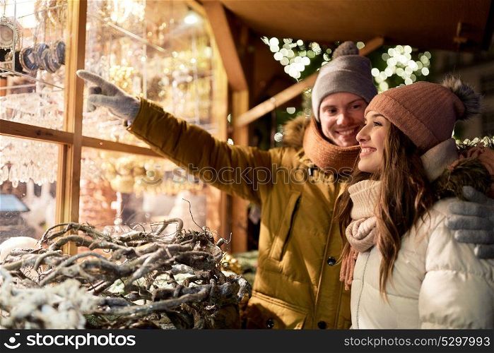 holidays, winter and people concept - happy couple at christmas market shop window in evening choosing souvenirs. happy couple at christmas market shop window