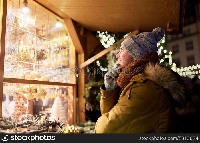 holidays, winter and people concept - happy man looking at christmas market shop window and choosing souvenir. happy man looking at christmas market shop window