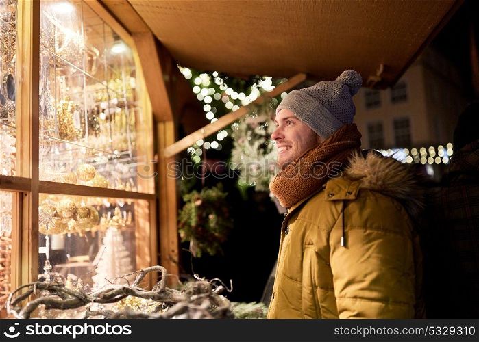 holidays, winter and people concept - happy man looking at christmas market souvenir store shop window. happy man looking at christmas market shop window