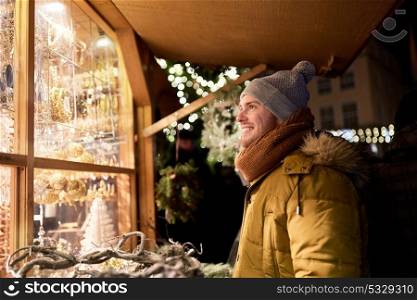 holidays, winter and people concept - happy man looking at christmas market souvenir store shop window. happy man looking at christmas market shop window