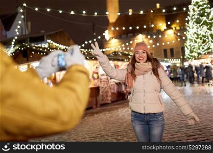 holidays, winter and people concept - happy woman posing for boyfriend with smartphone on square at christmas market. happy woman posing for smartphone at christmas