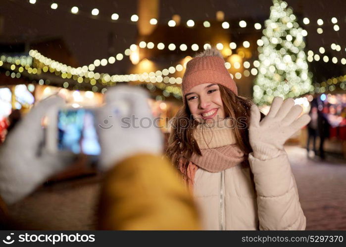 holidays, winter and people concept - happy woman posing for boyfriend with smartphone on square at christmas market. happy woman posing for smartphone at christmas