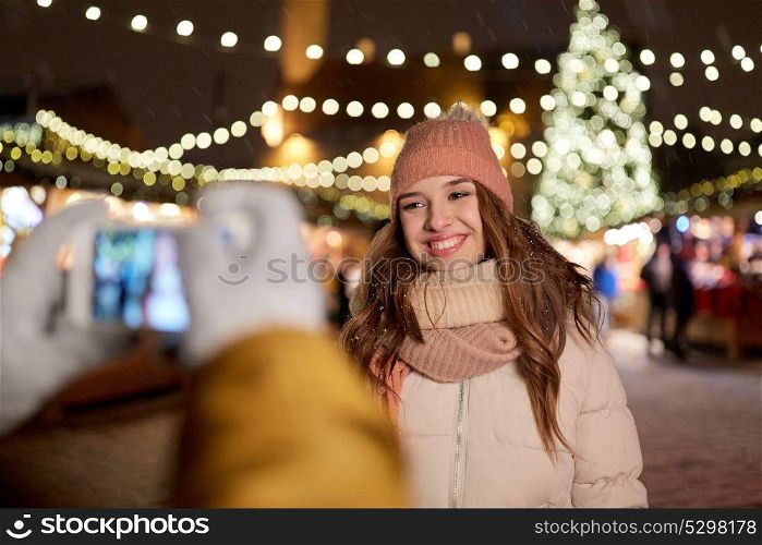 holidays, winter and people concept - happy woman posing for boyfriend with smartphone at christmas market. happy woman posing for smartphone at christmas