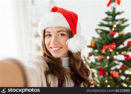 holidays, winter and people concept - happy young woman or teenage girl in santa hat over christmas tree at home