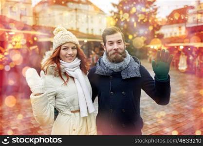 holidays, winter, christmas, gesture and people concept - happy couple of tourists in warm clothes waving hands in old town
