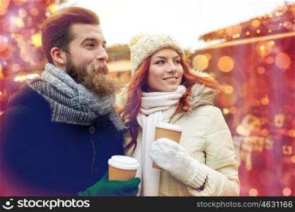 holidays, winter, christmas, hot drinks and people concept - happy couple of tourists in warm clothes drinking coffee from disposable paper cups in old town