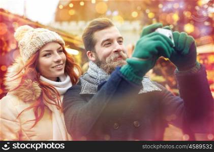 holidays, winter, christmas, technology and people concept - happy couple of tourists in warm clothes taking picture with camera in old town
