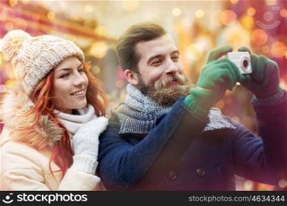 holidays, winter, christmas, technology and people concept - happy couple of tourists in warm clothes taking picture with camera in old town