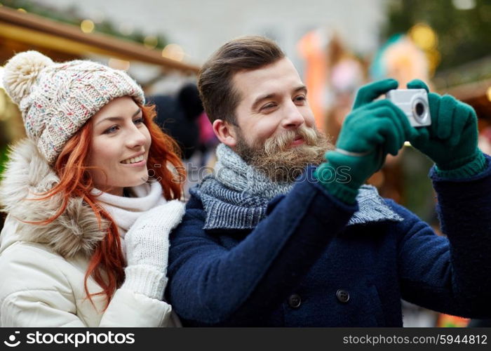 holidays, winter, christmas, technology and people concept - happy couple of tourists in warm clothes taking picture with camera in old town