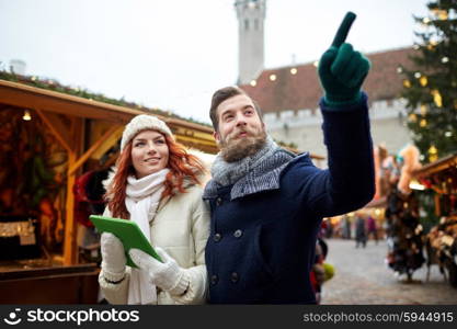 holidays, winter, christmas, technology and people concept - happy couple of tourists in warm clothes with tablet pc computer pointing finger in old town