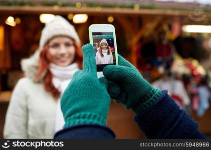 holidays, winter, christmas, technology and people concept - happy couple of tourists in warm clothes taking picture with smartphone in old town