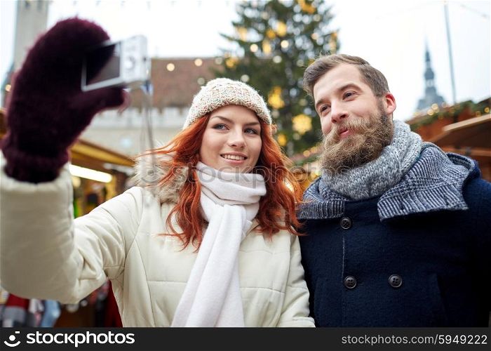 holidays, winter, christmas, technology and people concept - happy couple of tourists in warm clothes taking selfie with smartphone in old town