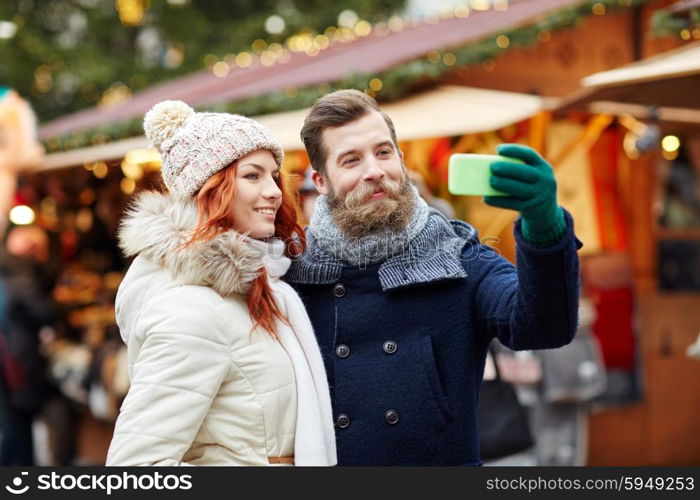 holidays, winter, christmas, technology and people concept - happy couple of tourists in warm clothes taking selfie with smartphone in old town