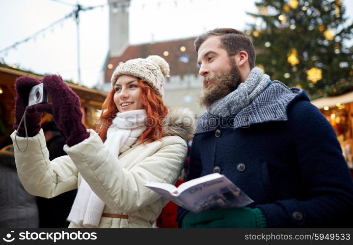 holidays, winter, christmas, technology and people concept - happy couple of tourists in warm clothes taking picture with smartphone in old town