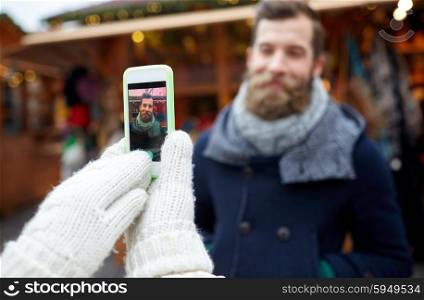 holidays, winter, christmas, technology and people concept - happy couple of tourists in warm clothes taking picture with smartphone in old town