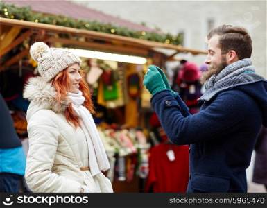 holidays, winter, christmas, technology and people concept - happy couple of tourists in warm clothes taking picture by smartphone or camera in old town