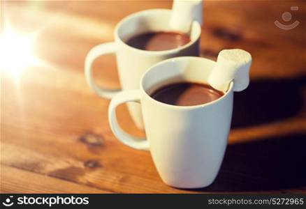 holidays, winter, food and drinks concept - close up of cups with hot chocolate or cocoa drinks and marshmallow on wooden table. cups of hot chocolate with marshmallow on wood