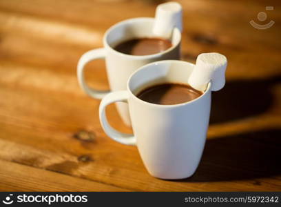 holidays, winter, food and drinks concept - close up of cups with hot chocolate or cocoa drinks and marshmallow on wooden table