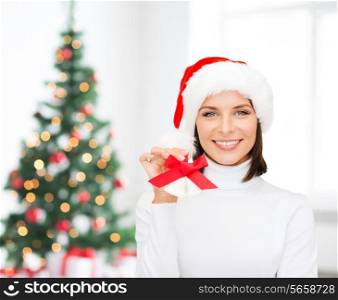 holidays, winter, happiness and people concept - smiling woman in santa helper hat holding jingle bells over room with christmas tree background